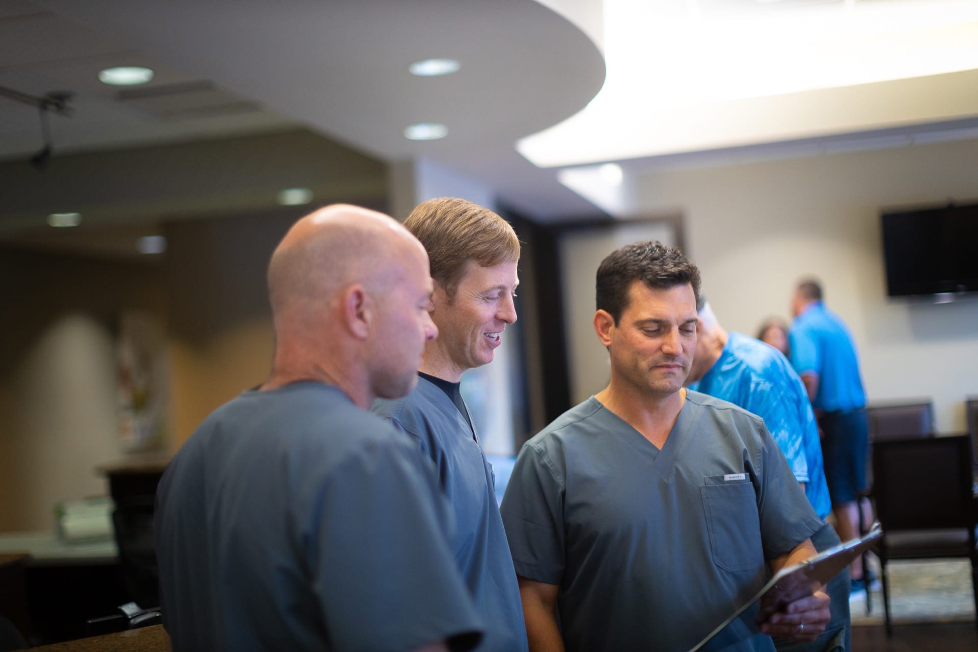 Three men in dark shirts conversing in a modern indoor facility with recessed lighting.