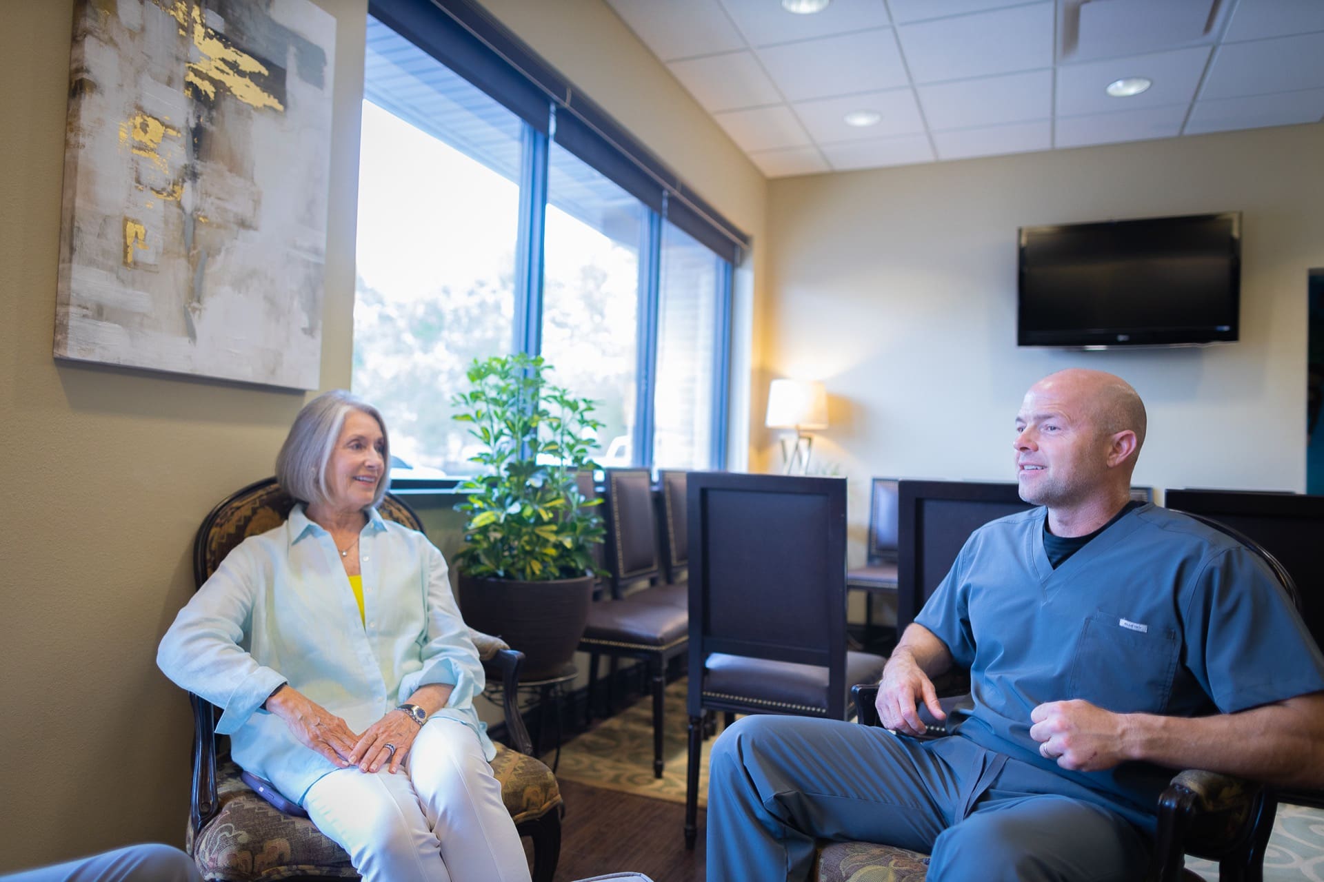 Two people having a conversation in a bright, modern office waiting area with large windows.