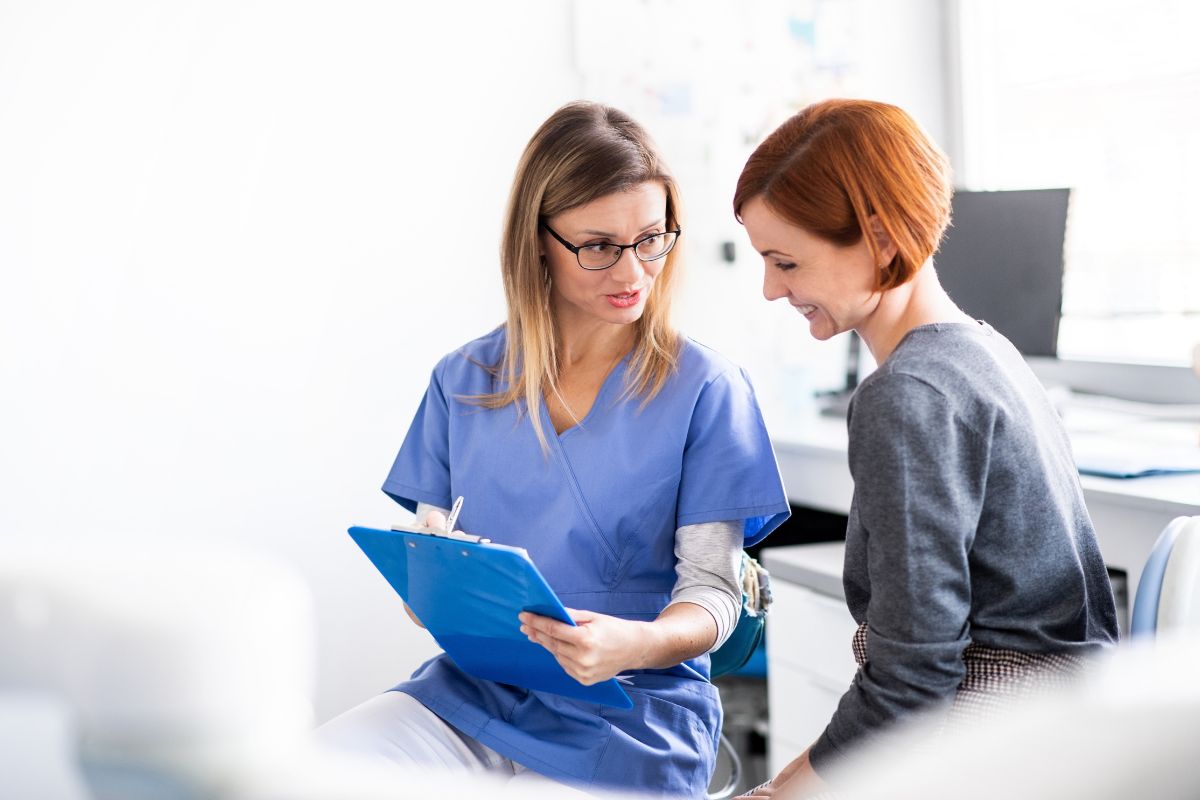 Healthcare professional in blue scrubs reviews medical document with patient in clinical office setting.