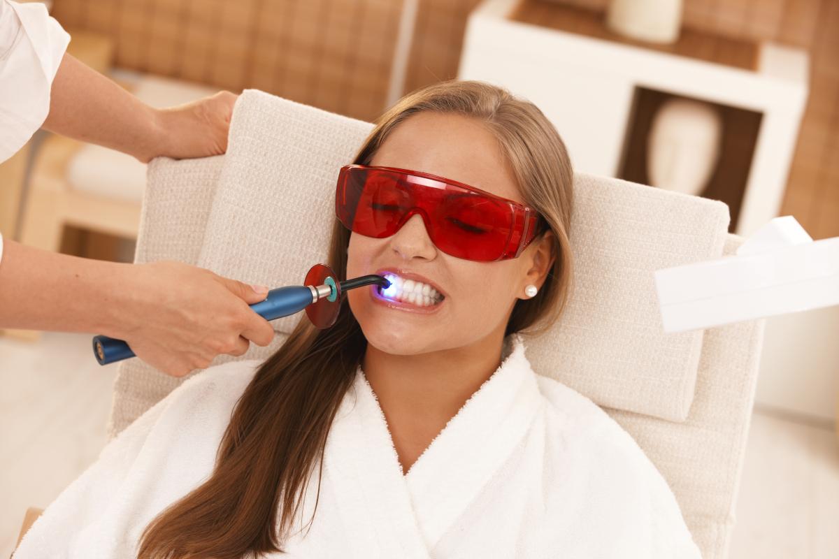 Woman wearing red protective eyewear receives dental treatment in modern clinic setting.
