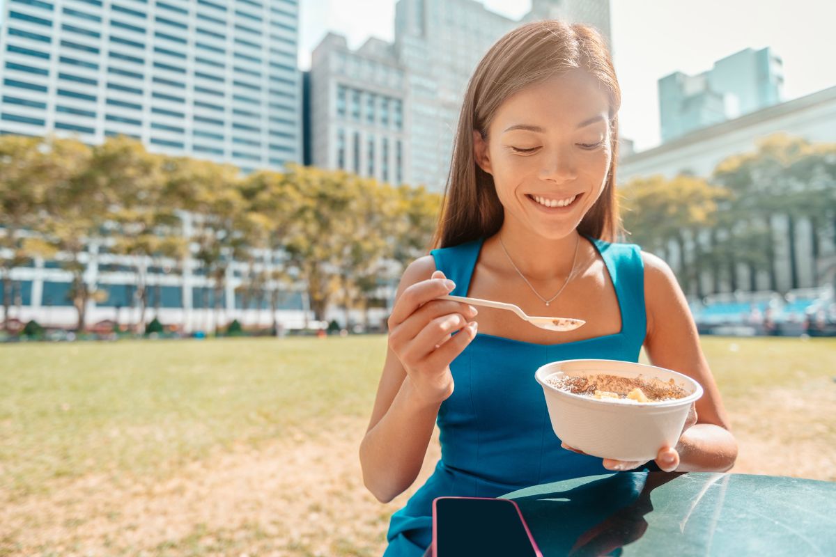 Girl eating noodles in park with city skyline and buildings in background