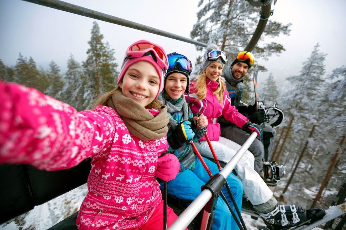 Children in winter gear skiing together on a snowy forest slope, smiling at camera.
