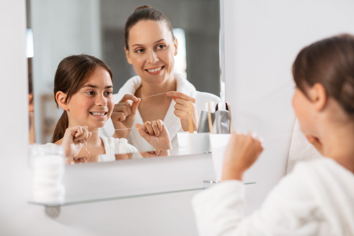 Mother and daughter brushing teeth together at bathroom mirror in morning routine.