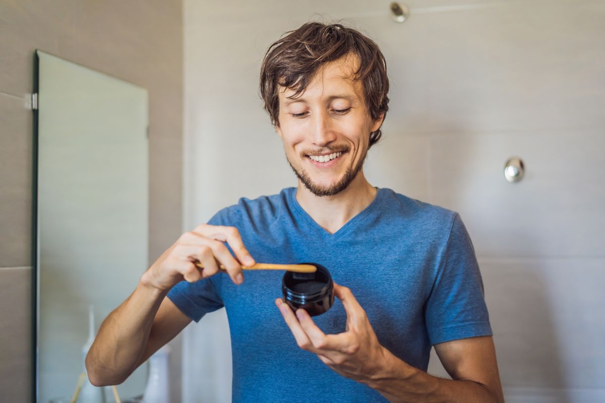 Man in blue shirt holding smartphone horizontally, smiling indoors against white wall.